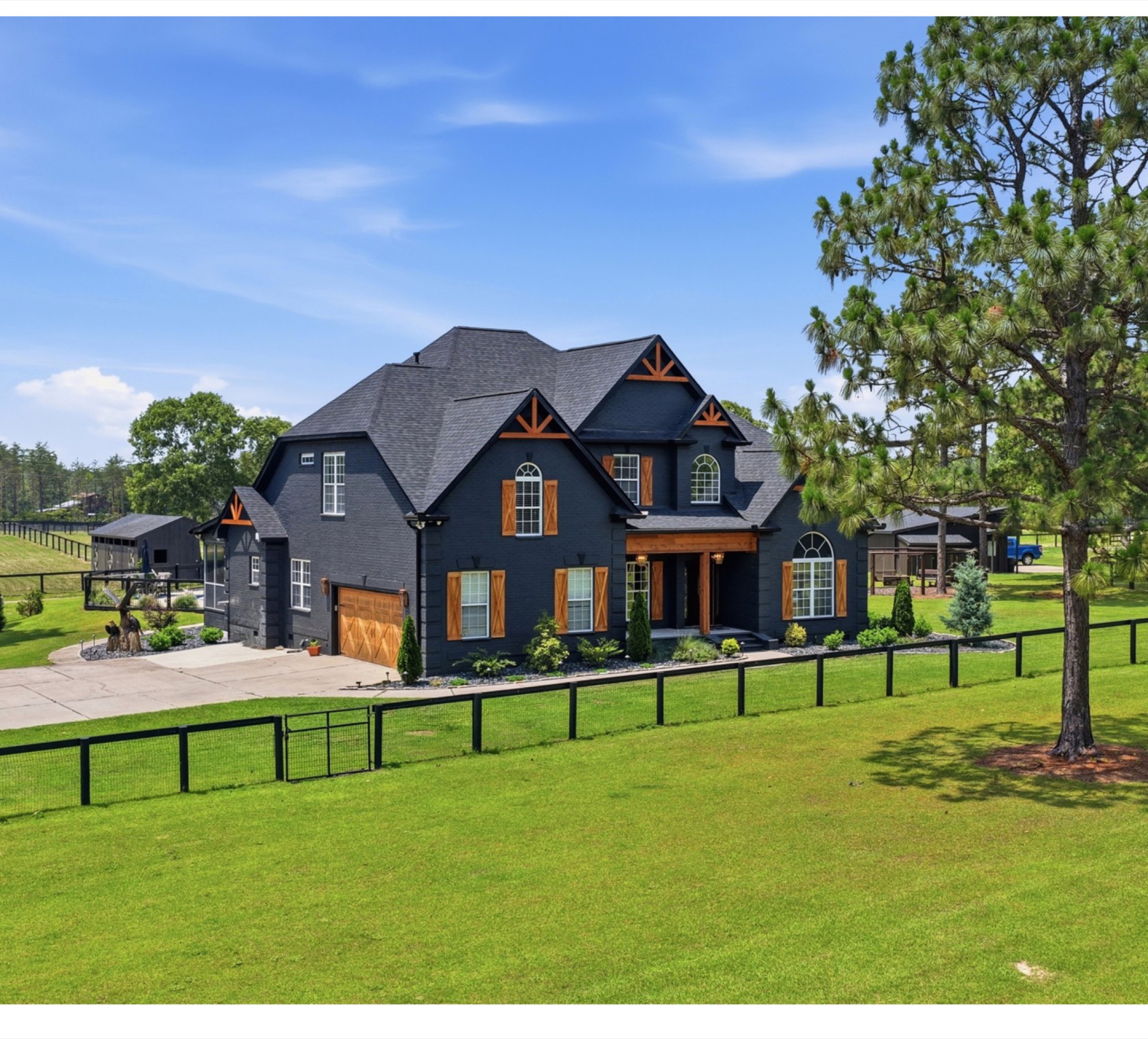 The home at 8520 Stock Horse Trail, seen from the front pasture, black board-and-batten with cedar accents behind a horse fence.
