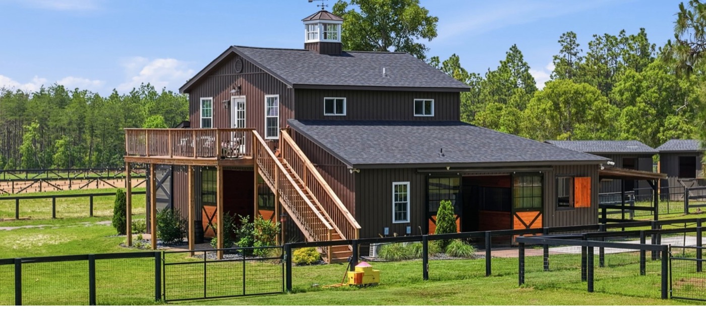 The barn complex at 8520 Stock Horse Trail, two storeys with a covered upper deck over the stalls.