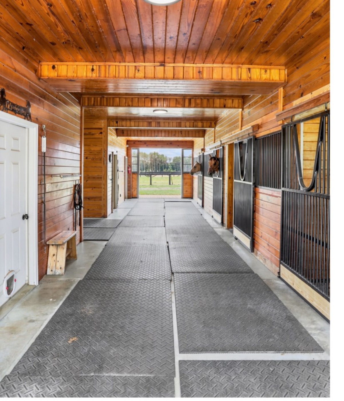 Wood-lined stall aisle at 8520 Stock Horse Trail with two horses looking out over their stall doors.
